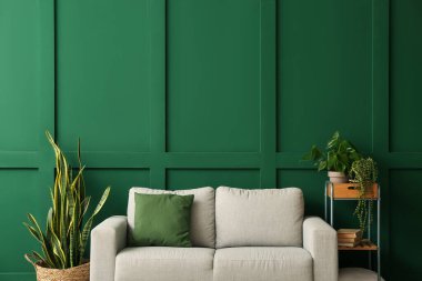 Yeşil duvarın yanında rahat bir kanepe ve bitkiler.