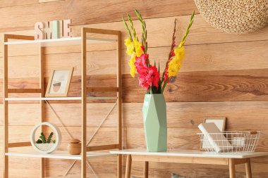 Üzerinde güzel gladiolus çiçekleri olan vazo ahşap duvarın yanında.