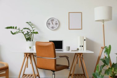 Diz üstü bilgisayarlı, saatli, aydınlık duvarlı modern işyeri