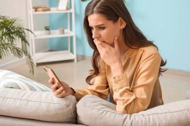 Evde cep telefonu mesajı okuyan endişeli genç bir kadın.
