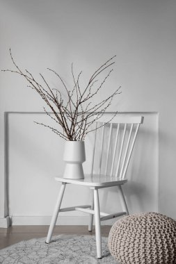 Sandalyesinde ağaç dalları olan vazo ve ışık duvarının yanında puf