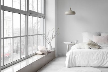 Beyaz duvarın yanında, aydınlık odanın içinde rahat bir yatak.