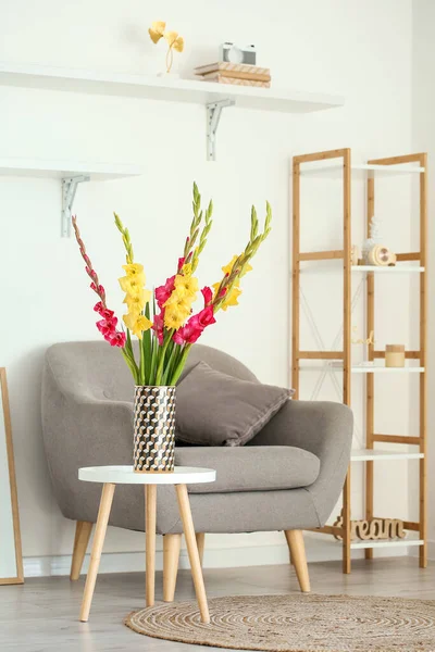 白い壁の近くのテーブルとアームチェアの上に美しいグラジオラスの花の花瓶 — ストック写真