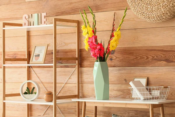 Üzerinde güzel gladiolus çiçekleri olan vazo ahşap duvarın yanında.