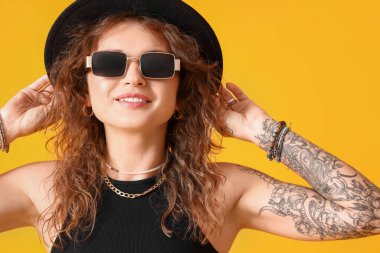 Sarı arka planda modaya uygun dövmeli kadın.