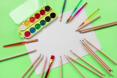 Renkli kalemler, boş kağıt kağıtlar ve yeşil arkaplanda fırçalı resimler.