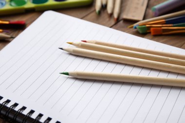 Renkli kalemler, boş defterler ve ahşap arka planda fırçalarla boyalar.