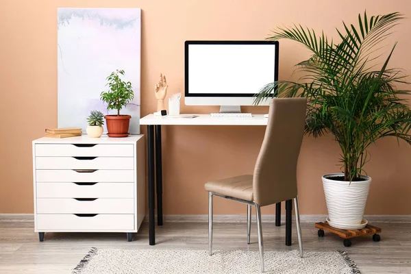 Interior of room with modern workplace and houseplant near color wall