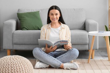 Diş teli takan güzel bir kadın evde dergi okuyor.