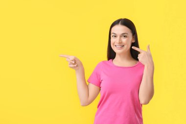 Beautiful woman with dental braces pointing at something on yellow background clipart