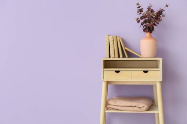 Okaliptüs dallı vazo ve menekşe duvarın yanındaki masada kitaplar.