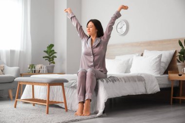 Genç Asyalı çıplak ayaklı kadın yatak odasında geriniyor.