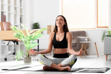 Genç çıplak ayaklı kadın evde meditasyon yapıyor.