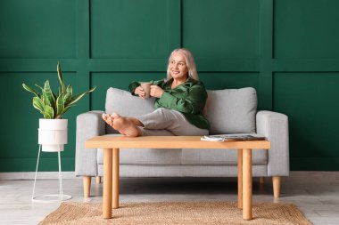 Yeşil duvarın yanında oturmuş çay içen olgun bir kadın.