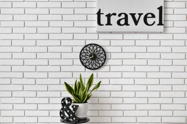 Odasında hafif tuğla duvarda asılı ev bitkisi ve modern saat olan masa.