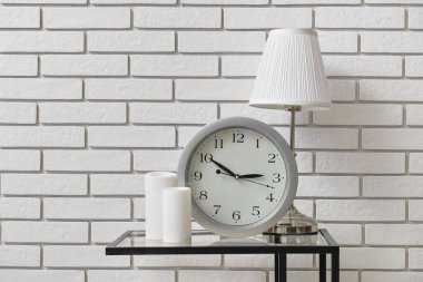 Modern saati, lambası ve mumları olan bir masa.