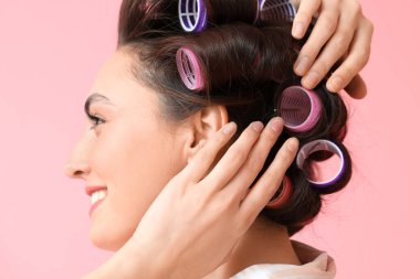 Pembe arka planda saç bigudileri olan güzel bir kadın.