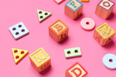 Ahşap küpler, pembe arkaplanda harfler ve bloklar.