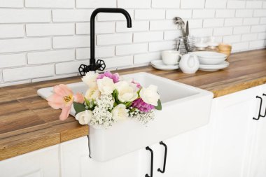 Beyaz tuğla duvarın yanındaki tezgahta güzel çiçeklerle lavabo