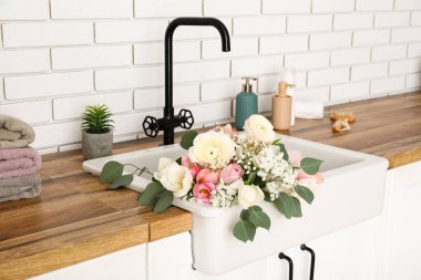 Güzel çiçeklerle lavabo ve banyo malzemeleri beyaz tuğla duvarın yanındaki tezgahlarda.