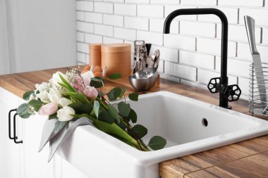 Güzel çiçekli lavabo ve mutfak malzemeleri beyaz tuğla duvarın yanındaki tezgahlarda, yakın plan.