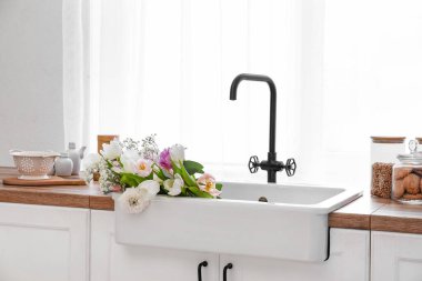 Mutfağın penceresinin yanındaki tezgahta güzel çiçeklerle lavabo.