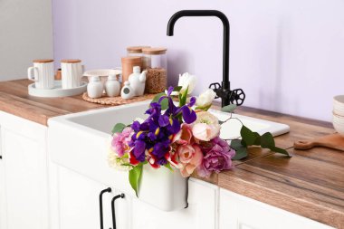 Güzel çiçeklerle lavabo ve mutfak malzemeleri leylak duvarın yanındaki tezgahlarda.