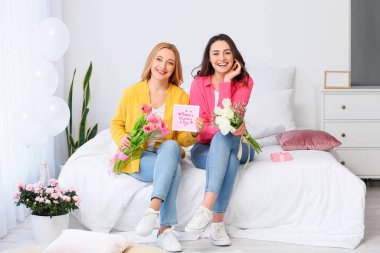 Evde Uluslararası Kadınlar Günü için çiçek ve tebrik kartıyla genç bir kadın ve annesi var.