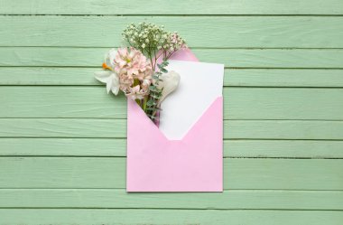 Yeşil ahşap zemin üzerinde kart ve çiçekler olan zarf