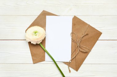 Beyaz ahşap zemin üzerinde boş kart ve çiçek içeren zarflar