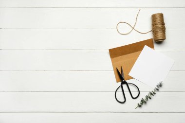 Beyaz tahta zemin üzerinde boş kart, okaliptüs dalı, ip ve makas ile zarf