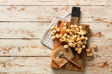 İçinde kızarmış ekmek, kaşık, parşömen kağıdı ve ahşap arka planda peçete olan tahta.