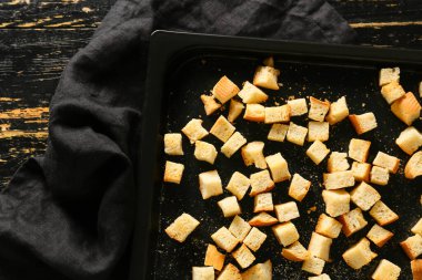 Lezzetli kıtır ekmekler ve koyu ahşap arka planda peçeteyle pişirme tabağı.