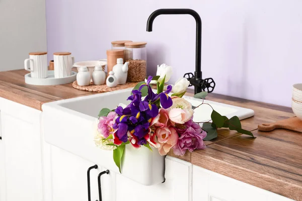 Güzel çiçeklerle lavabo ve mutfak malzemeleri leylak duvarın yanındaki tezgahlarda.
