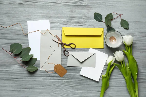 Envelopes with cards, candle, scissors, tulips and eucalyptus leaves on grey wooden background