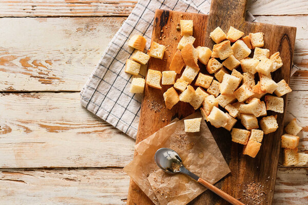 Board with croutons, spoon, parchment paper and napkin on light wooden background