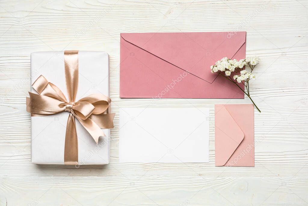 Envelopes with card, flowers and gift on white wooden background