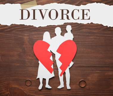 Aile figürü, kırık kağıt kalp ve tahta arka planda alyanslar. Boşanma kavramı