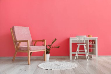Şık pembe koltuklu ev bitkisi ve odanın içindeki renkli duvarın yanındaki sandalyeli masa.