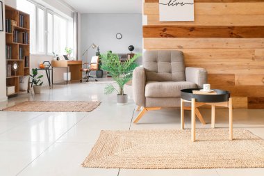 Koltuğu, masası ve hasır halısı olan modern bir oda.