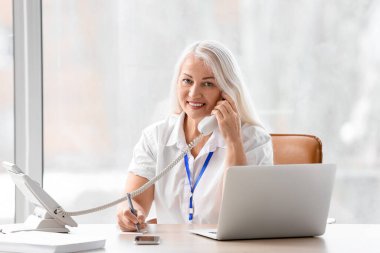 Ofiste çalışırken telefonla konuşan olgun sekreter.