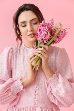 Pembe arka planda sümbül çiçekleri olan güzel genç bir kadın.