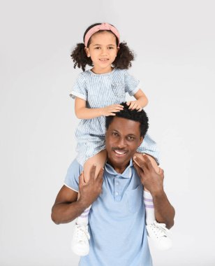 Küçük Afro-Amerikalı bir kızın portresi gri arka planda babasının omuzlarında oturuyor.