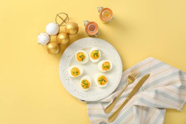 Sarı arka planda içi doldurulmuş yumurta, çatal bıçak, peçete ve baharatla dolu bir tabak. Paskalya kutlaması