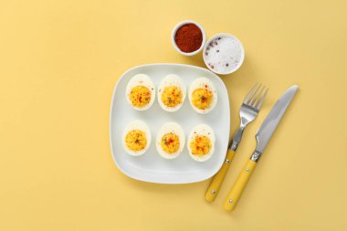 Sarı arka planda içi doldurulmuş yumurta, çatal bıçak ve baharatla dolu bir tabak. Paskalya kutlaması