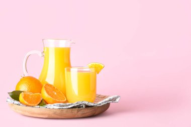 Pembe arka planda bir sürahi taze mandalina suyu.