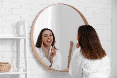 Güzel genç bir kadın banyoda dişlerini kömür diş macunuyla fırçalıyor.