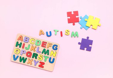 Pembe arkaplanda bulmaca parçaları ve harfleri olan kelime AUTISM