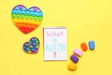 Metin içeren defter AUTISM nedir?, sarı arka planda oyuncak ve plastikçeyi oynat