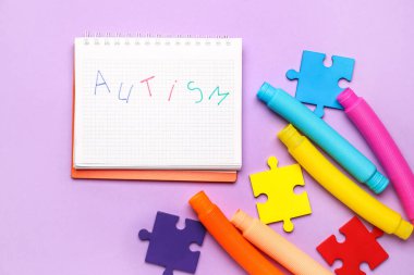 Kelimesi kelimesine AUTISM, bulmaca parçaları ve leylak arkaplanda pop tüpleri olan bir defter.